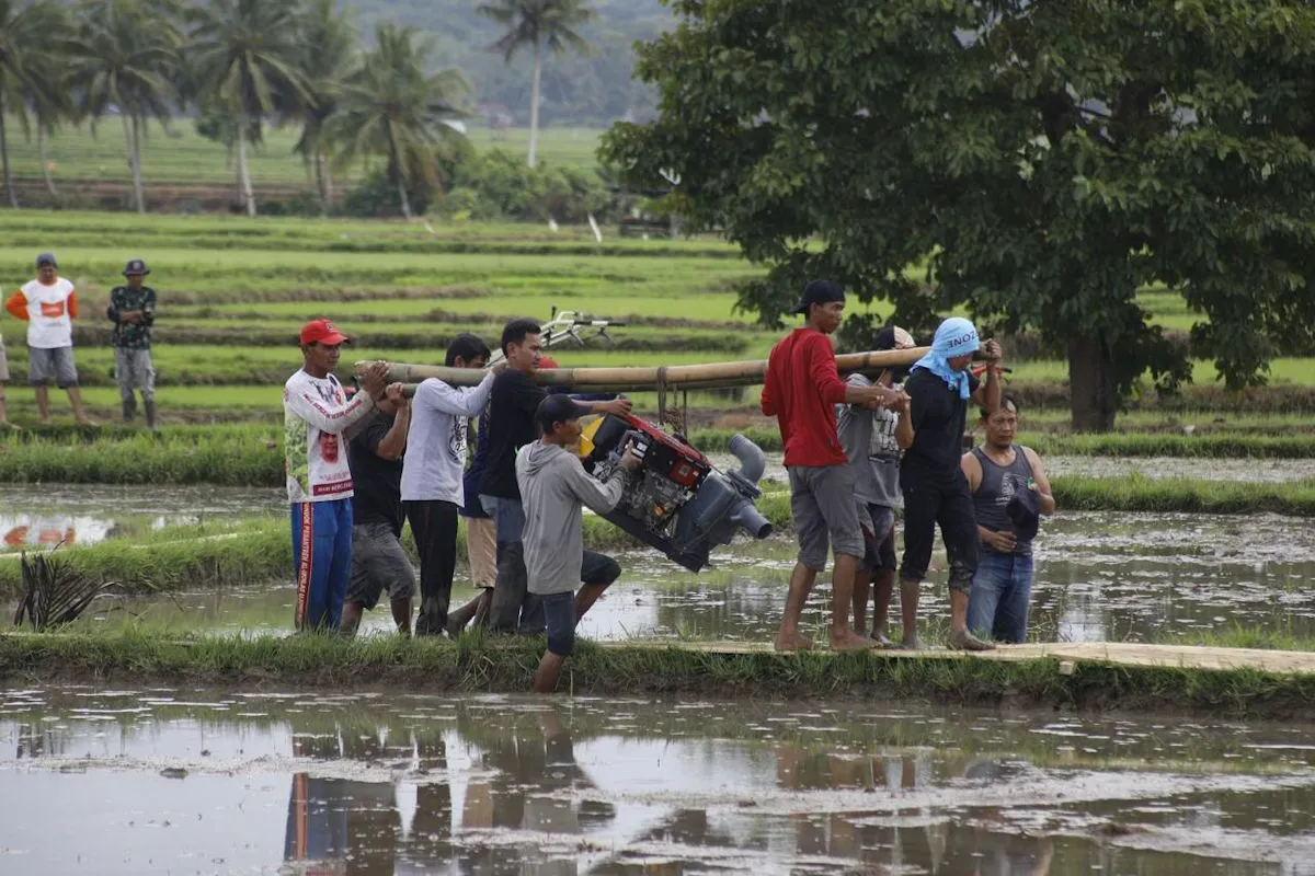 Petani menggotong pompa air menuju areal persawahan sebagai upaya menjaga ketersediaan air irigasi, mempertahankan produktivitas padi, dan memitigasi dampak kekeringan selama musim kemarau.