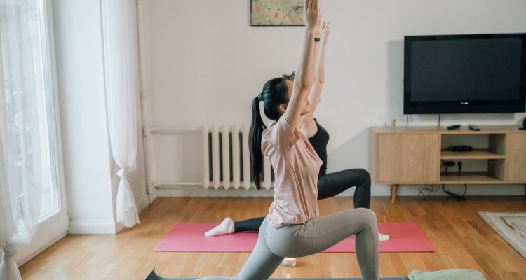 Dua perempuan melakukan gerakan yoga di rumah untuk menjaga kebugaran dan melatih fleksibilitas tubuh.