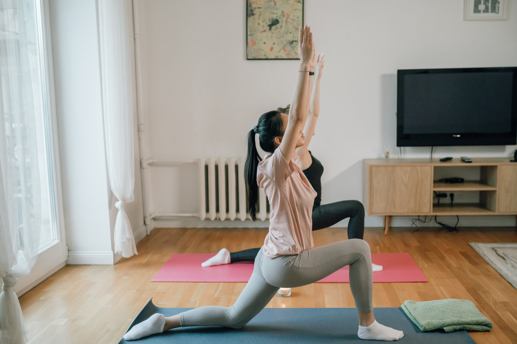 Dua perempuan melakukan gerakan yoga di rumah untuk menjaga kebugaran dan melatih fleksibilitas tubuh.
